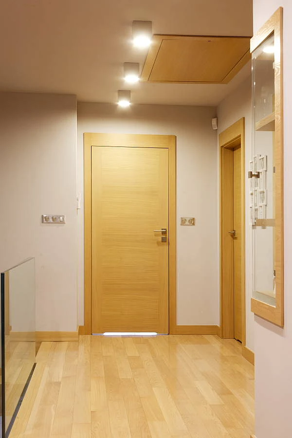 Jasne drewniane drzwi do łazineki wpasowujące się do przedpokoju. 