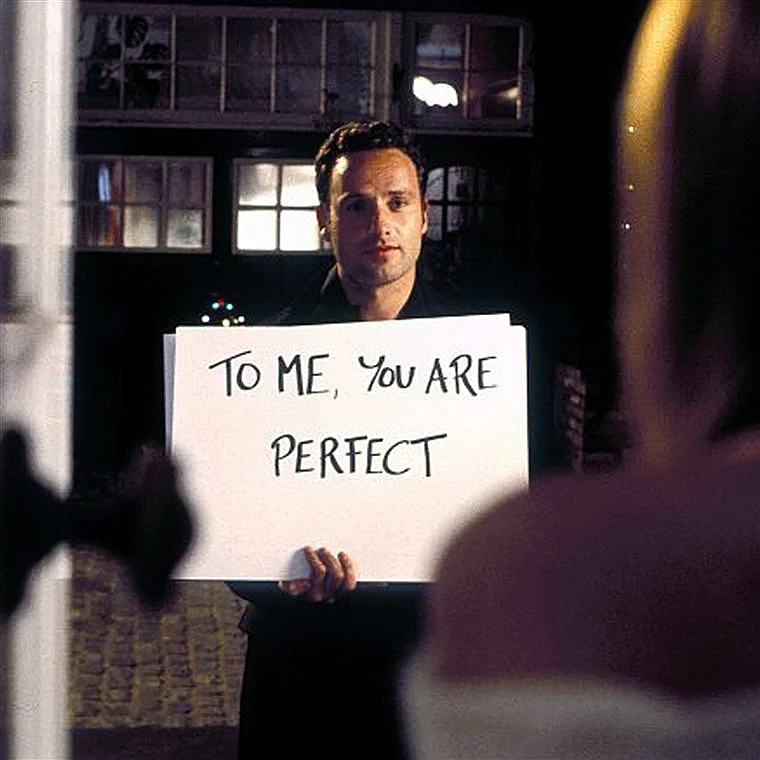 Kadr z filmu „To właśnie miłość”, na którym jeden głównych bohaterów trzyma tablicę z napisem „To me, you are perfect”.