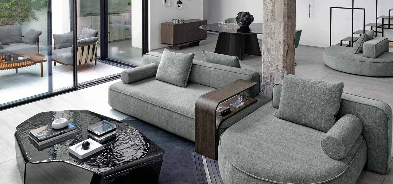 Szara, dużej wielkości sofa w kolorze szarym z drewnianym podłokietnikiem w salonie inspirowanym stylem industrialnym