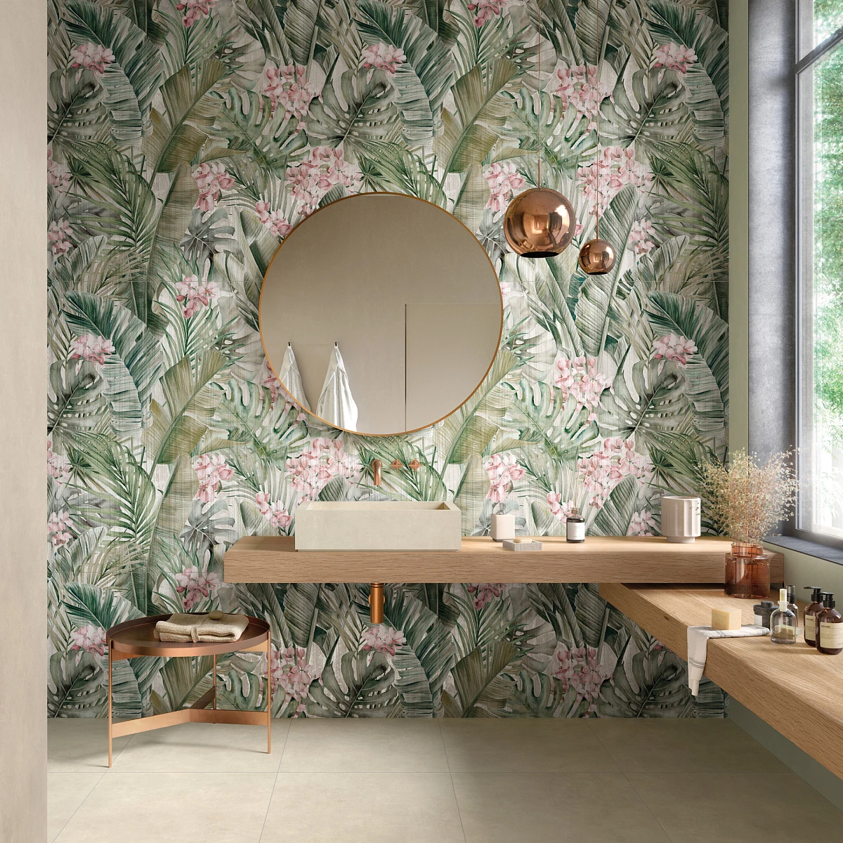 Tapeta z motywem roślinnym w delikatnym zielonym kolorze, znajdująca się za blatem łazienkowym oraz okrągłym lustrem. 