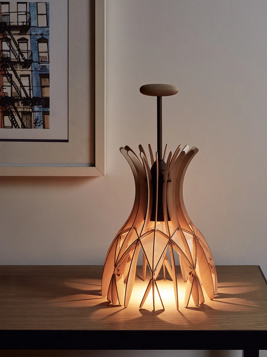 Niewielka, drewniana, designerska lampa stojąca na drewnianym stole. 