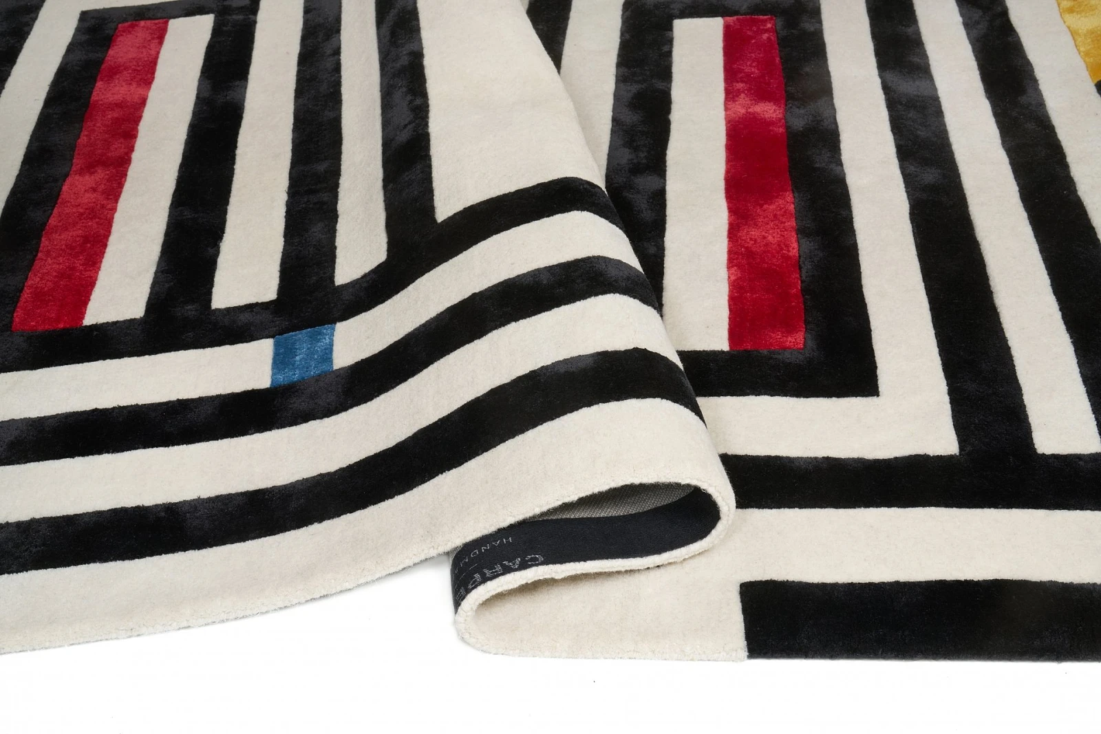Kremowy dywan z czarnym wzorem przypominającym labirynt, z dodatkowymi czerwonymi, niebieskimi i żółtymi elementami.